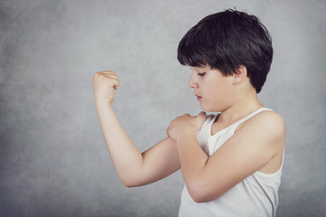 niño fuerte que enseña sus músculos sobre fondo gris