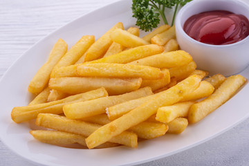 French fries fried in oil with salt, spicy ketchup in a white plate
