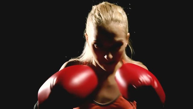 Slow motion of boxer shadow boxing. Young white woman in black background. Fighting sport fitness concept.