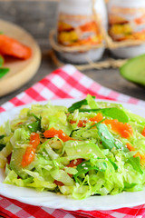 Easy avocado cabbage coleslaw. Diet cabbage salad with fresh avocado, dried apricots, arugula and sesame on a plate and on a wooden table. Healthy comfort food for vegetarians and vegans. Closeup