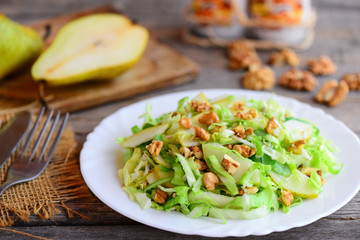 Cabbage and pear salad. Easy salad with fresh pear, cabbage and walnuts on a white plate and on rustic wooden background. Comfort food salad. Healthy meal. Closeup