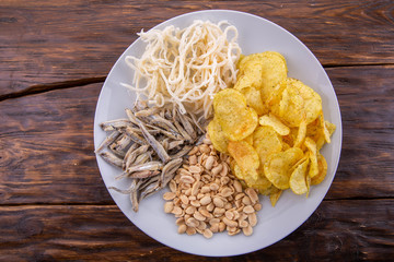 A plate with snack, peanut, a small fish, squids, chips on a dark wooden background