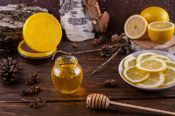 A honey jar with lemon segments on a dark wooden background with natural cones and bark