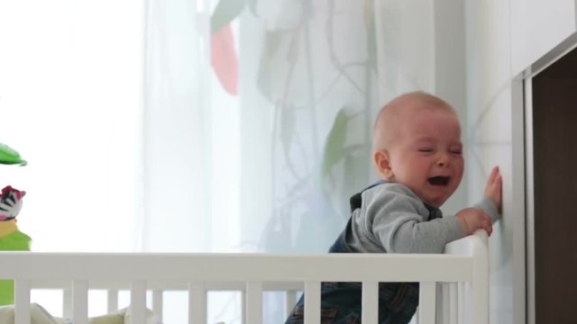 Sad baby boy, crying in crib at home
