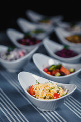 Salads in white plates on the table. Salad from cabbage, tomatoes and greens in the foreground. In the blurry background, there are other different salads.