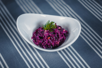 Top view of a salad in the white plate on the table with a blue tablecloth in white strips.