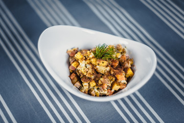 Top view of a salad in the white plate on the table with a blue tablecloth in white strips.
