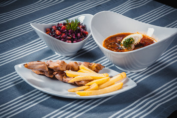 Set of three dishes. Business lunch of three dishes. Three dishes on white plates on a table with a blue tablecloth striped. Soup, salad and hot dish.