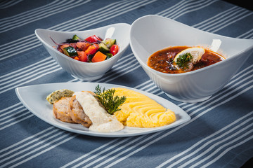 Set of three dishes. Business lunch of three dishes. Three dishes on white plates on a table with a blue tablecloth striped. Soup, salad and hot dish.