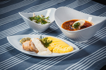 Set of three dishes. Business lunch of three dishes. Three dishes on white plates on a table with a blue tablecloth striped. Soup, salad and hot dish.