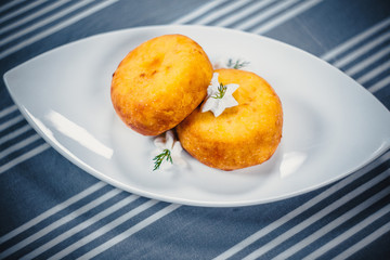 Top view of two patties or kartoplyanik on a white plate. Plate on the table with a blue tablecloth in white strips.