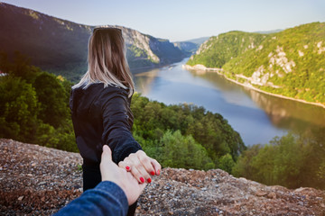 Naklejka premium the girl is holding the hand of the guy is walking forward, rear view. landscape and mountains and river