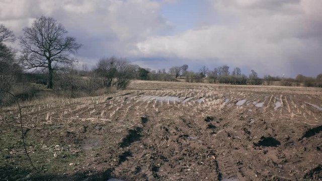 Muddy rural landscape with dirt and mud in field, Tarvin, Cheshire, England, UK. Overcast sky with trees in background. Clouds move fast
