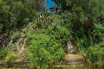 Close-up of a waterfall and a sunny blue sky at the Gardens of the Fountain, in the city center of Nimes. Located in the Gard department, Occitanie region in southern France