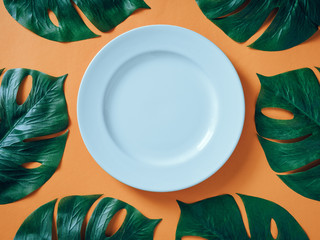 White ceramic plate with tropical leaves Monstera on orange background. flat lay, top view
