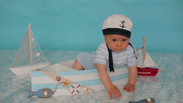 Cute toddler baby boy in wooden boat, playing with fishes, starfish and binoculars as sailman, studio indoors shot