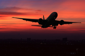 Commercial airplane flying over the night scene city on beautiful sunset background