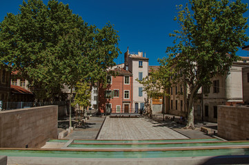 Quiet square with pond, trees, buildings and blue sky in the city center of Nimes. Located in the...