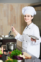 Professional female cook holding ladle by stove with pot