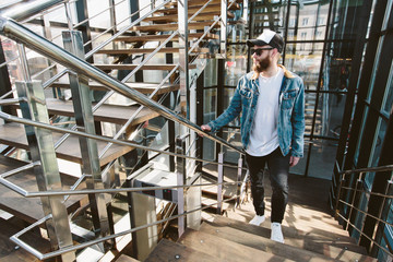 Hipster handsome male model with beard wearing white blank t-shirt and a baseball cap with space for your logo or design in casual urban style