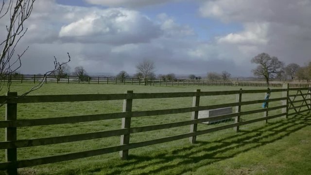 Rural landscape with green grass meadow behind timber fence, Tarvin, Cheshire, England, UK. Overcast sky in background