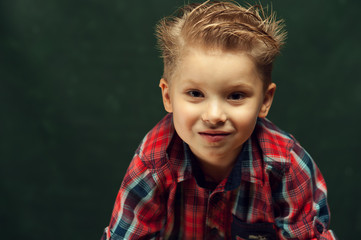 Portrait of positive little boy- an elementary school student laughing against dark background