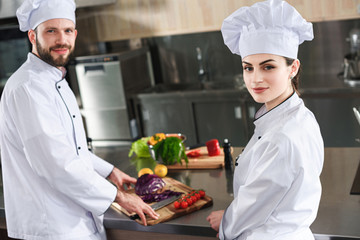 Professional chefs looking at camera by table with cooking ingredients