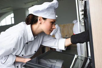 Woman cook checking baking oven in restaurant kitchen