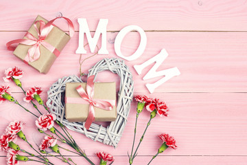 Mother's Day background with carnation flowers and gift boxes on pink wooden table. Top view.