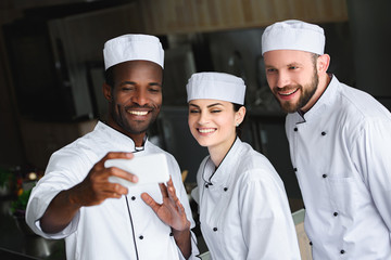 multicultural chefs taking selfie with smartphone at restaurant kitchen