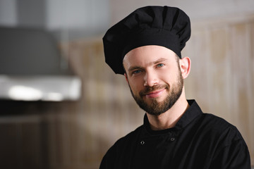 portrait of handsome chef in black uniform looking at camera at restaurant kitchen