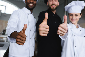 cropped image of smiling multicultural chefs showing thumbs up at restaurant kitchen