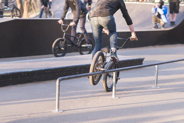 Naklejka premium Two cyclists on BMX bikes do tricks in a park skate. Bike skater slides on BMX by perel. Training of tricks on BMX