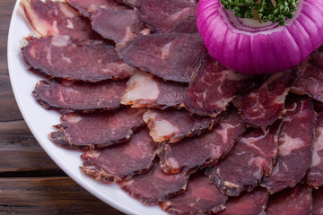 Smoked pieces of meat on a plate with red onions and greens