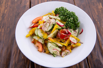 Vegetables oil and greens salad, is served in a white plate on a dark wooden background