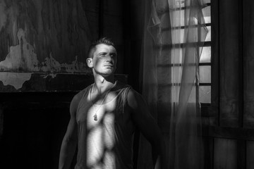 Young handsome guy near window lit by dramatic sunlight