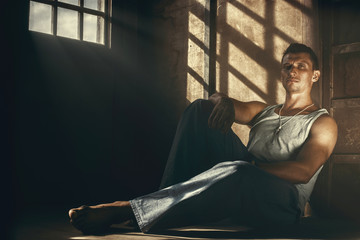 Young handsome guy sitting on the floor lit by dramatic sunlight.