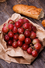 A bunch of juicy large red grapes and fresh crispy wheaten baguette on a table of dark old wooden boards