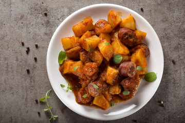Potatoes stew with pork sausage slices and tomato sauce on a white plate
