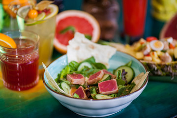Salads from fresh products with meat, fish, chicken and vegetables on the table among colorful refreshing cocktails with ice.