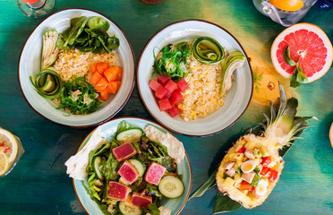 Salads from fresh products with meat, fish, chicken and vegetables on the table among colorful refreshing cocktails with ice.