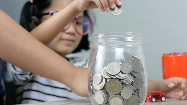 Asian little girl putting the coin in to a glass jar shallow depth of field select focus on jar