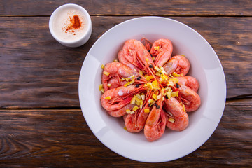 The shrimps fried on a white plate with lemon sauce and segments of a lemon on a dark wooden background