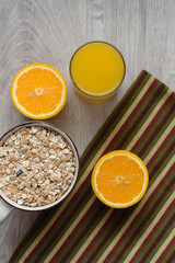 Still life healthy breakfast of muesli, oranges and orange juice in a glass, striped napkin on a wooden background.