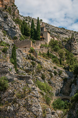Fototapeta na wymiar View of the church Notre-Dame de Beauvoir amid the cliffs and houses of the charming village Moustiers-Sainte-Marie. In the Alpes-de-Haute-Provence department, Provence region, southeastern France