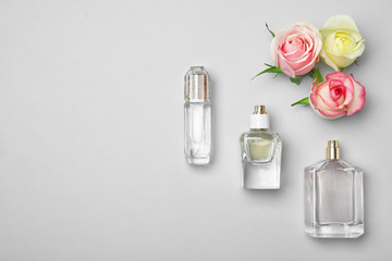 Bottles of perfume and roses on light background, top view