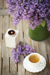 Green vase with Lilac flower, candle light and cup of porcelain coffee  on wooden table at the outdoor garden