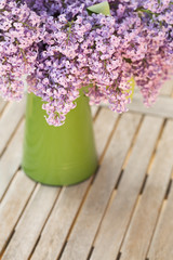 Fresh and romantic lilac in green vase on wooden background with copy space