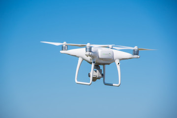 The modern drone, quadrocopter is in the air against the background of the sky and grass