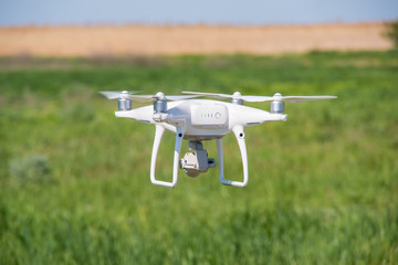 The modern drone, quadrocopter is in the air against the background of the sky and grass